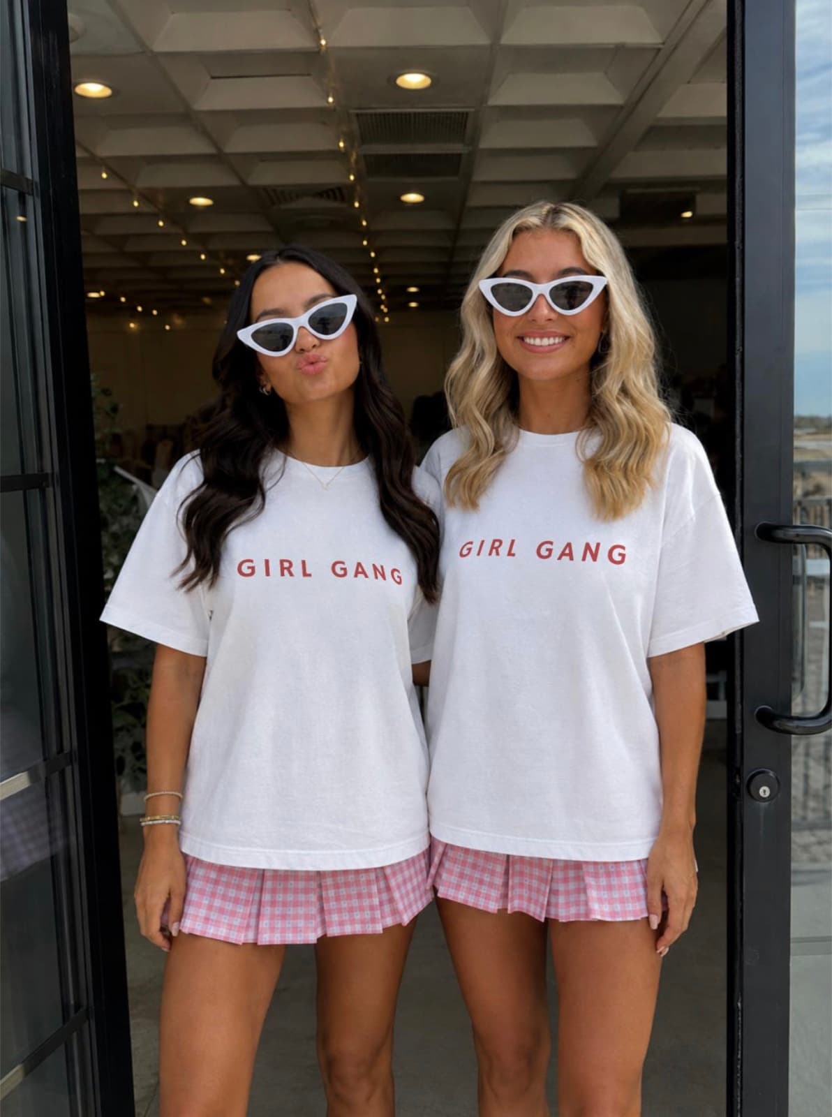 Two friends posing in matching Girl Gang tees, sunglasses and pink shorts